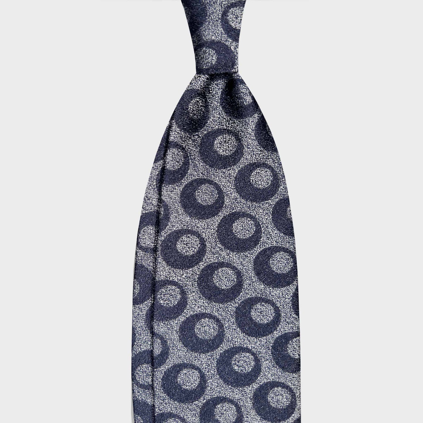 Art Decò Silk Tie Melange Navy Blue Wools Boutique Uomo Geneva. Refined navy blue silk tie with an Art Deco geometric pattern on a melange silver background. A sophisticated accessory for elegant tailoring.