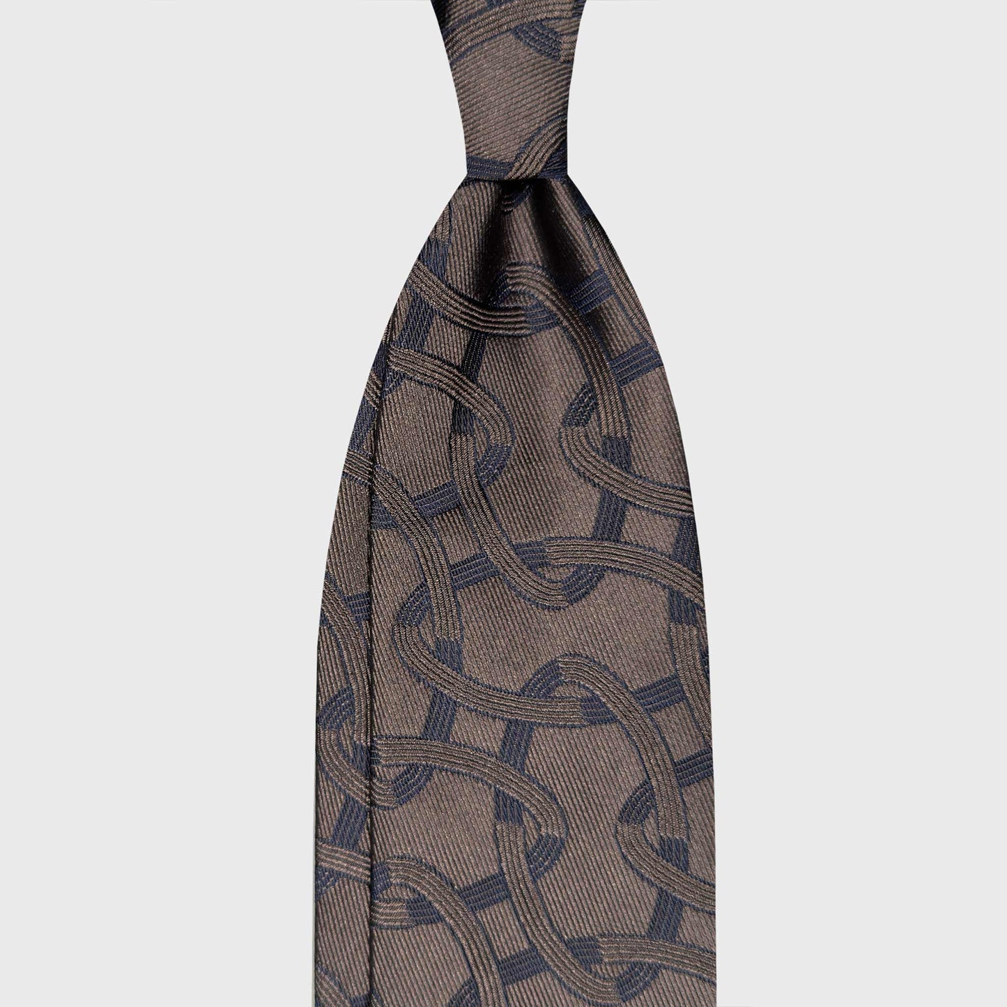Bronze Brown Art Déco Silk Tie Geneva Luxury Men Accessories. Art Déco silk tie with an oval chain pattern in bronze brown and navy blue. Handmade in Italy and selected by Wools Boutique Uomo Geneva.