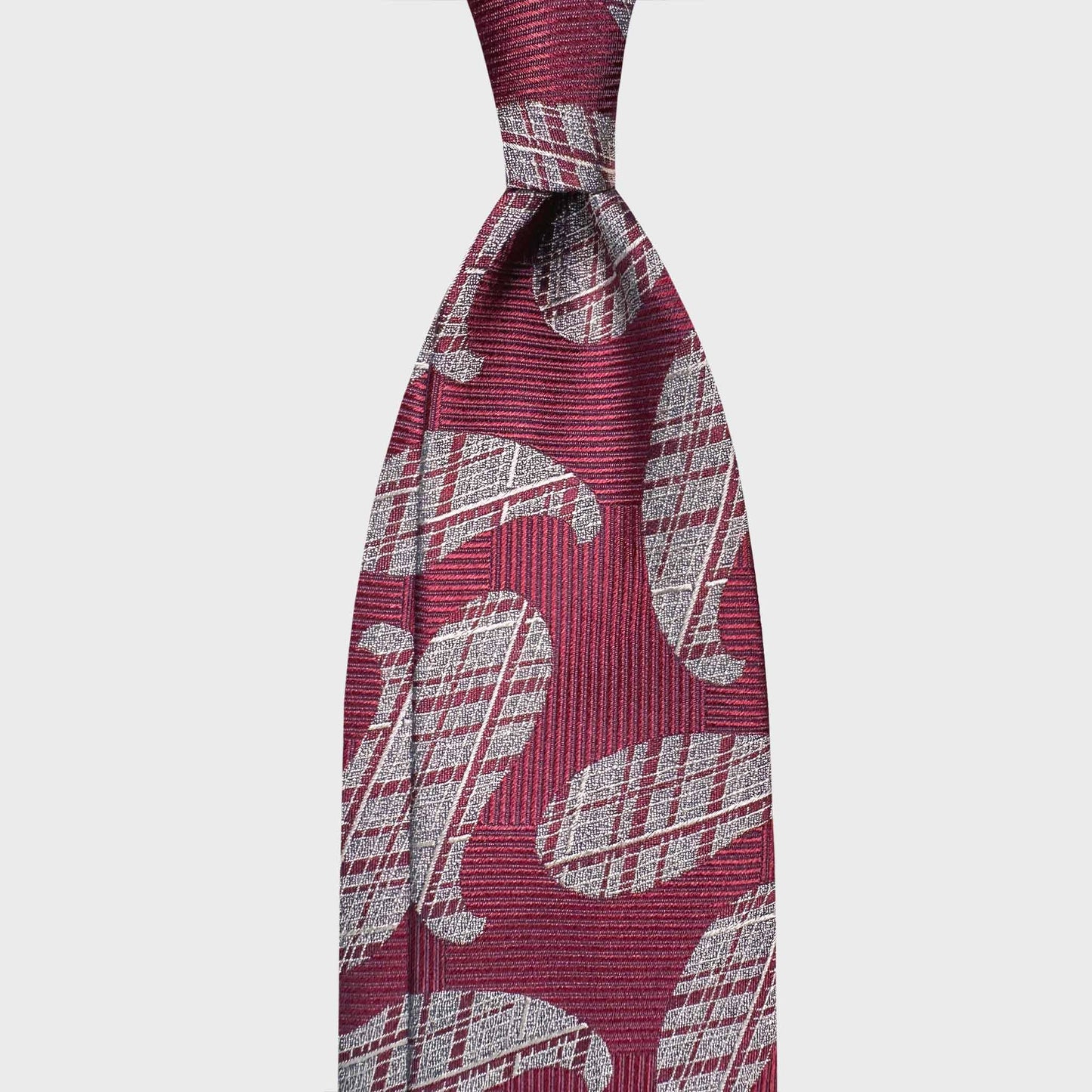Ruby red silk tie featuring large silver paisley motifs with refined woven texture. A heritage-inspired statement piece crafted in Italy, ideal for elegant formal wear and distinctive sartorial styling.