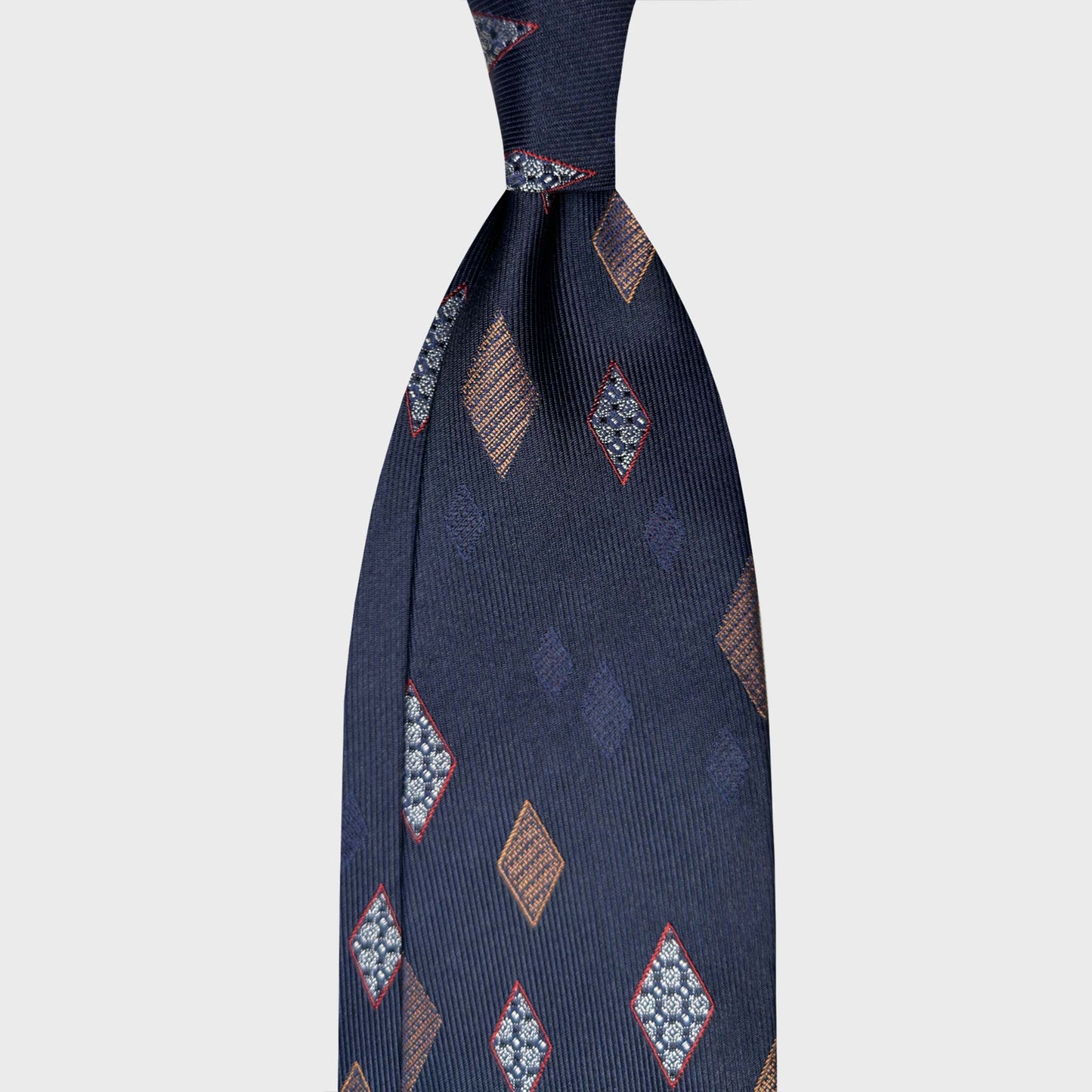 Navy blue silk tie featuring classic diamond medallions in light blue and bronze tones. A refined Italian design ideal for elegant business attire and sophisticated professional styling. Wools Boutique Uomo men's ties store in Geneva.